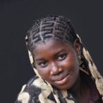 Portrait of a smiling young woman with braided hair against a dark background.